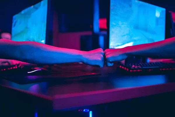 A young player seated in a red-and-black gaming chair at his station in a neon-lit room