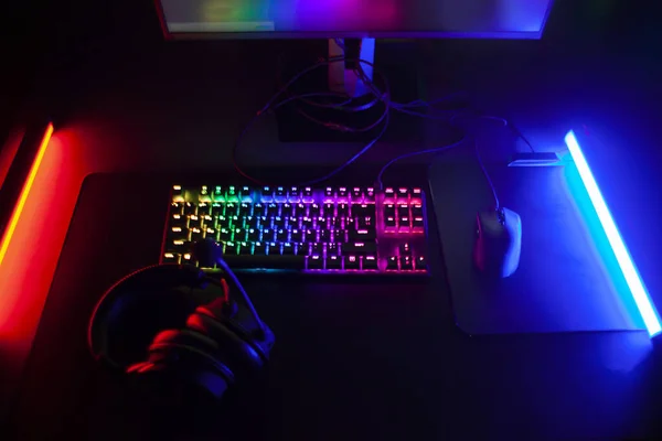 Top-down view of a gaming desk with an RGB-backlit mechanical keyboard, mouse and headset between neon light bars
